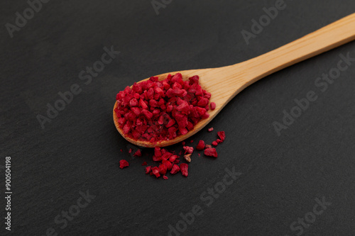 Crunchy pieces of Freeze dried raspberries in wooden spoon, close-up. Selective focus. Dehydrated raspberry berries. Delicious fruit topping for porridge, cereal, yogurt and desserts