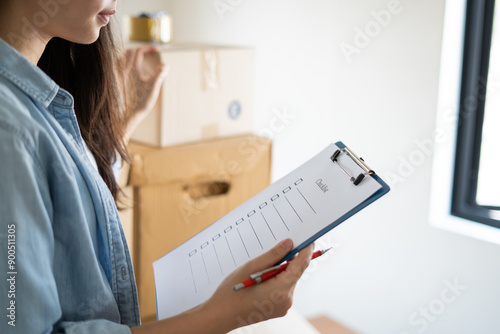 Asian woman checking and packing the carton box prepare to move to new house relocation shipping or check goods package before delivery to customer from online shopping by checklist photo