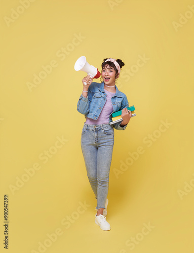 Young Asian student woman shouting into megaphone making announcement in isolated on yellow background.