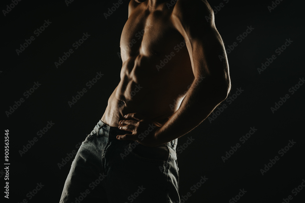 Fit muscular male torso in dramatic lighting showcasing defined abs and strong arms for fitness and health concepts. Fit muscular male torso in dramatic lighting showcasing defined abs and strong arms for fitness and health concepts.