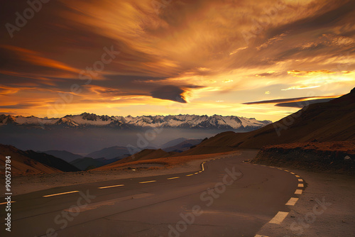 Mountain road winding through a dramatic sunset landscape with snow-capped peaks in the background