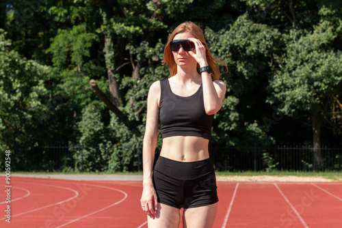 Young sport woman in black spot clothing and sunglasess standing on a running track. 