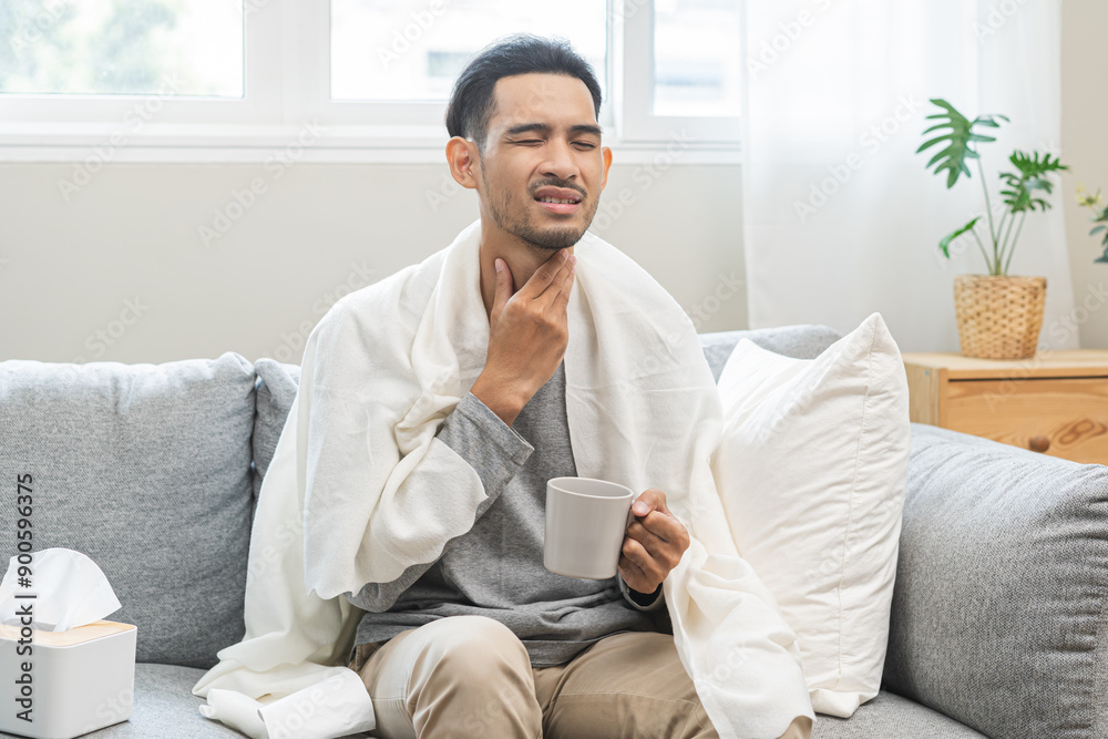 Sick, hurt asian young man sore throat have a fever, flu touching massage pain neck. Painful male drinking hot water of glass while sitting on sofa at home. Health care influenza with virus seasonal. Sick, hurt asian young man sore throat have a fever, flu touching massage pain neck. Painful male drinking hot water of glass while sitting on sofa at home. Health care influenza with virus seasonal.