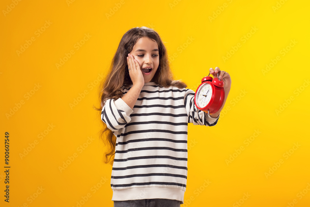 Surprised kid girl holding an alarm clock in hand. The concept of education, school, deadlines, time to study Surprised kid girl holding an alarm clock in hand. The concept of education, school, deadlines, time to study