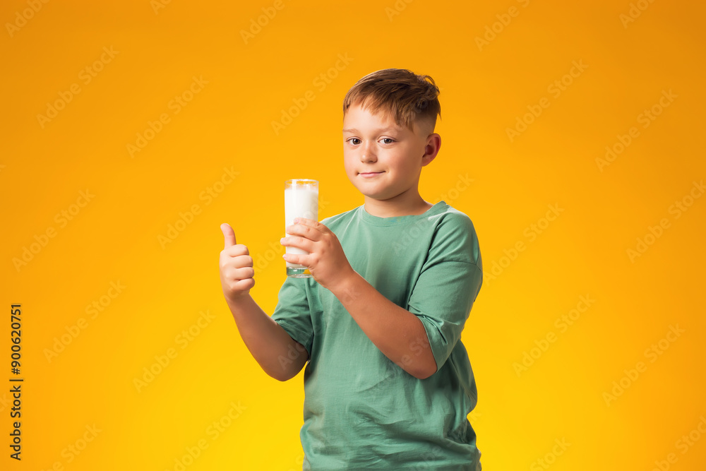 Child boy holding glass of milk and showing thumb up gesture over yellow background. Healthy food concept Child boy holding glass of milk and showing thumb up gesture over yellow background. Healthy food concept