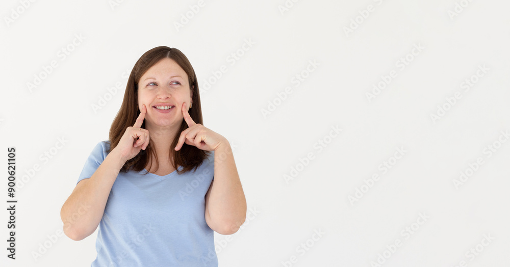 Young brunette woman pointing fingers at her cheeks isolated over white background Young brunette woman pointing fingers at her cheeks isolated over white background