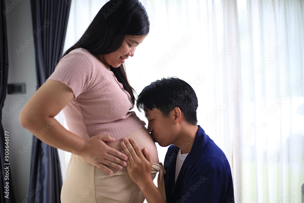 Happy man with pregnant wife rubbing his belly while relaxing and spending time in modern apartment. Pregnant woman and husband spending time together using smartphone Happy man with pregnant wife rubbing his belly while relaxing and spending time in modern apartment. Pregnant woman and husband spending time together using smartphone