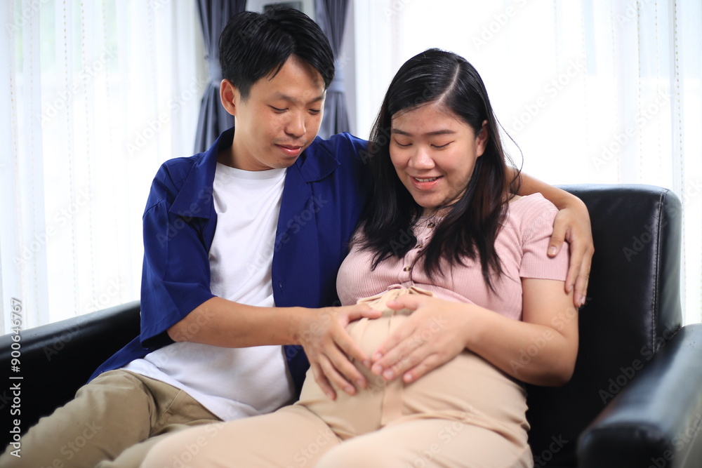 Happy man with pregnant wife rubbing his belly while relaxing and spending time in modern apartment. Pregnant woman and husband spending time together using smartphone Happy man with pregnant wife rubbing his belly while relaxing and spending time in modern apartment. Pregnant woman and husband spending time together using smartphone