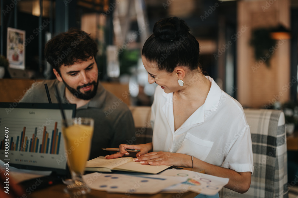 Two businesspeople discussing charts and data during a productive meeting at a coffee bar, with a laptop and documents on the table.