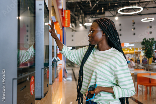 Quadro em tela Black Woman with glasses and striped shirt using a touch screen kiosk in a modern shopping mall
