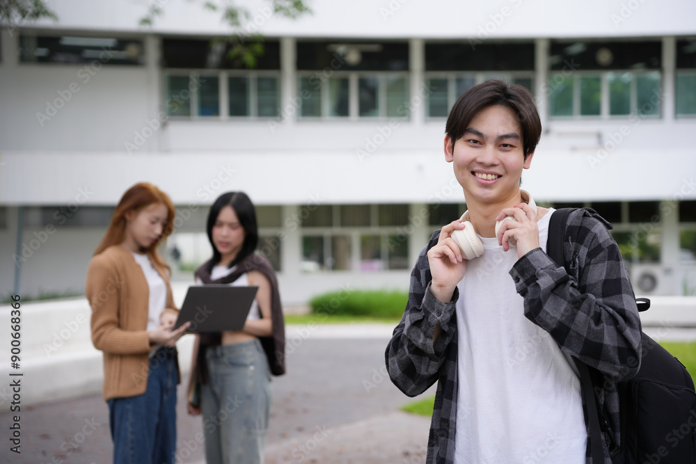 Fototapeta premium Smiling asian student holding headphones with friends studying on background in university campus