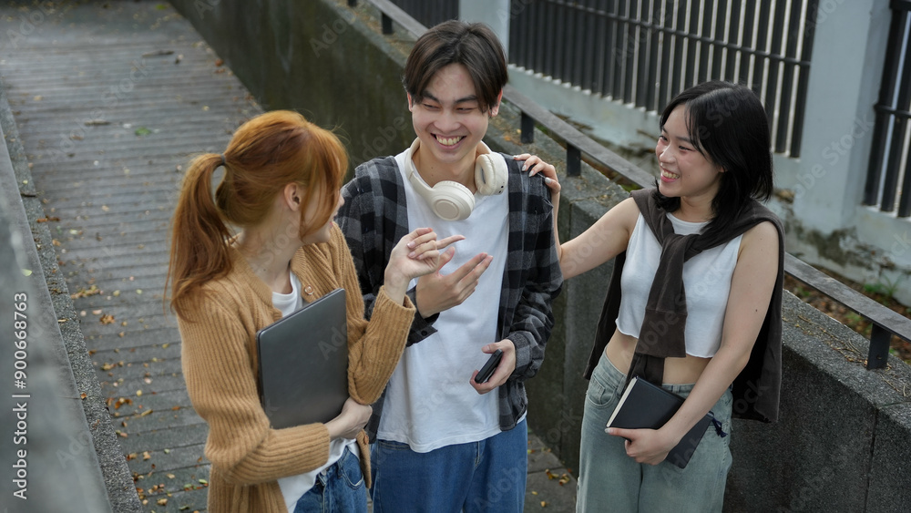 Three young people are standing on a campus walkway, talking and laughing together between classes Three young people are standing on a campus walkway, talking and laughing together between classes