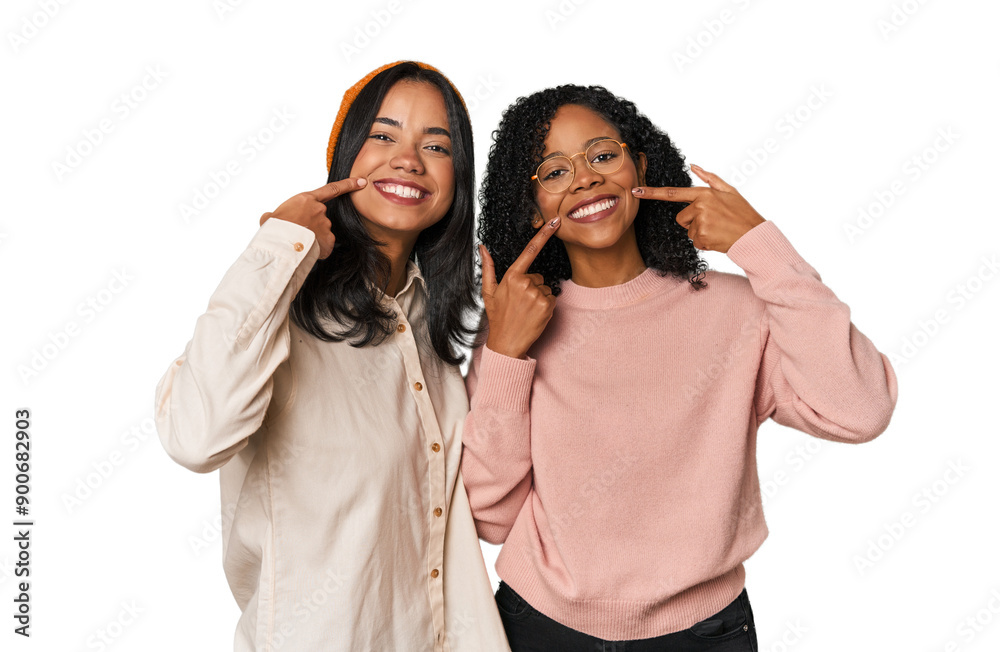 Young Latin friends together in studio smiles, pointing fingers at mouth. Young Latin friends together in studio smiles, pointing fingers at mouth.