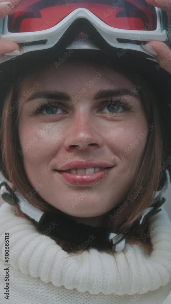 A beautiful Caucasian girl puts a white ski or snowboard helmet on her head. Portrait of a pretty woman at a winter resort. The female wears an orange protective mask or red glasses over her eyes. A beautiful Caucasian girl puts a white ski or snowboard helmet on her head. Portrait of a pretty woman at a winter resort. The female wears an orange protective mask or red glasses over her eyes.