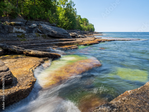 Smooth, silky water flowing over sun lit cliffs with moss by Lake Ontario, Robert G. Wehle State Park upstate New York, with horizon line and blue sky. photo