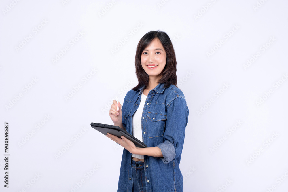 An Asian woman wearing denim jean is holding a tablet and a stylus against a white background. An Asian woman wearing denim jean is holding a tablet and a stylus against a white background.