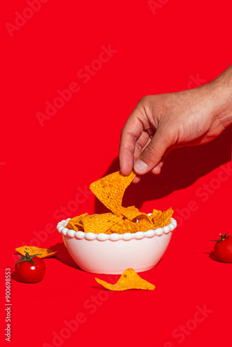 Picking tortilla chips from dish on isolated red background