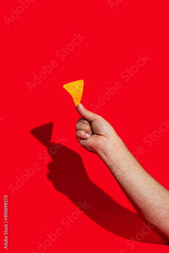 Hand with tasty tortilla chips or nachos with fresh homemade guacamole and tomato dip sauce on red background