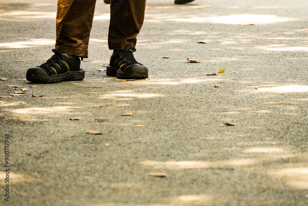 A person is standing on a sidewalk with their feet on the ground. The person is wearing a pair of shoes and has a backpack on. The scene is sunny and bright, with the sun shining down on the sidewalk A person is standing on a sidewalk with their feet on the ground. The person is wearing a pair of shoes and has a backpack on. The scene is sunny and bright, with the sun shining down on the sidewalk