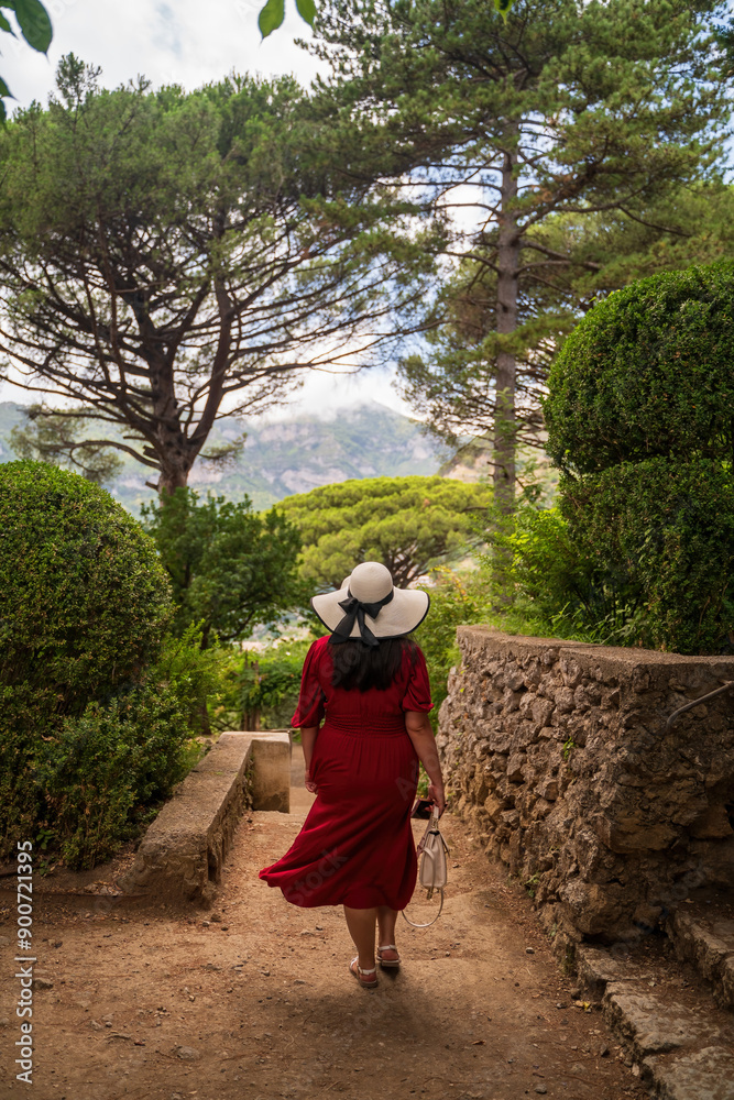 Woman in Red Dress and Hat Strolling Through a Scenic Garden
