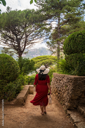 Woman in Red Dress and Hat Strolling Through a Scenic Garden