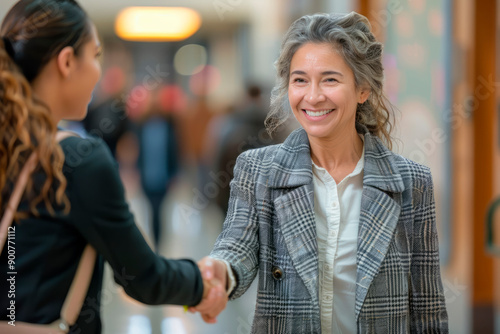 Teacher woman Hispanic 50 years old in gray jacket and white shirt shaking hand girl college student indoors