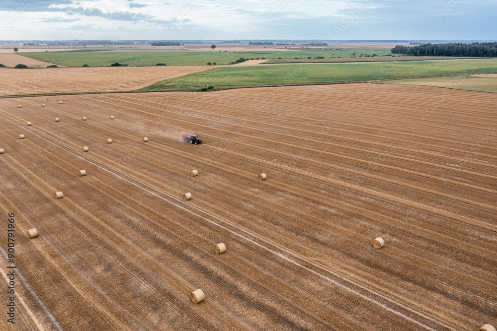 Obraz premium Aerial view of a agro-cultural field after harvesting and baler presses straw into bales