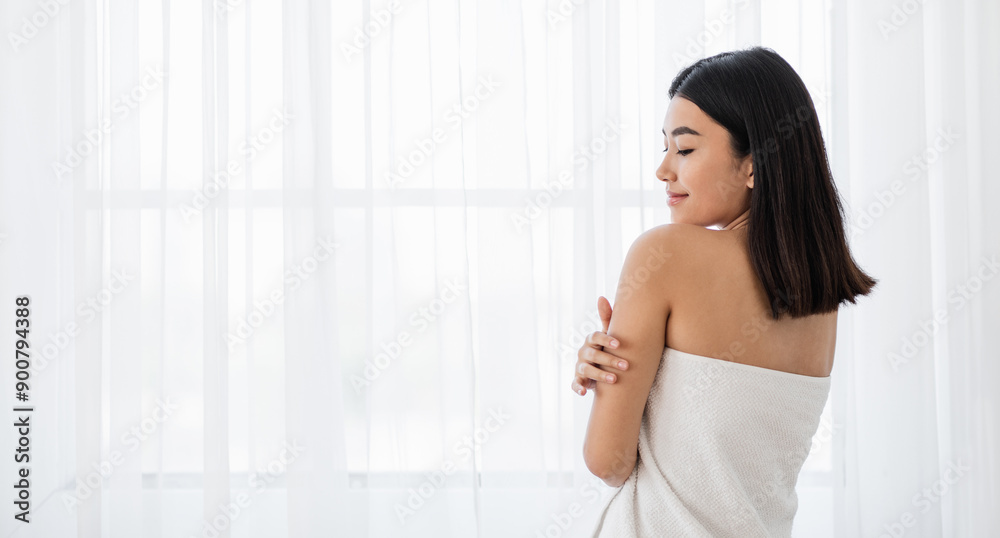 Joyful asian lady in towel touching her skin while standing by window at home. Young woman wrapped in white bath towel enjoying her soft skin after morning shower, panorama with copy space Joyful asian lady in towel touching her skin while standing by window at home. Young woman wrapped in white bath towel enjoying her soft skin after morning shower, panorama with copy space