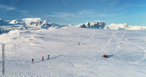 People enjoy outdoor sport activity in Antarctica. Group of scientists from polar station run snow trail race. Travel, active lifestyle, recreation in arctic wild nature landscape. Aerial drone shot