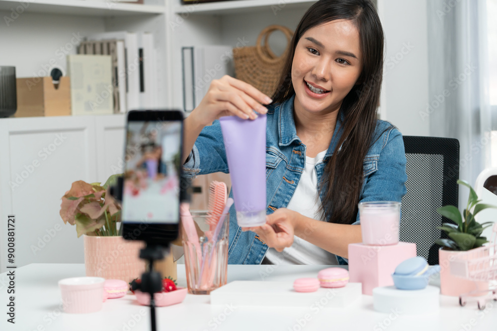 Young beautiful Asian girl reviewing moisturizing body lotion cream product to make glow skin testing on arm on social media online live recording smartphone with bestseller at modern room. Stratagem. Young beautiful Asian girl reviewing moisturizing body lotion cream product to make glow skin testing on arm on social media online live recording smartphone with bestseller at modern room. Stratagem.