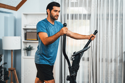 Billede på lærred Athletic and sporty man running on elliptical running machine during home body workout exercise session for fit physique and healthy sport lifestyle at home