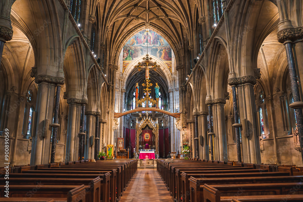 Fototapeta premium Grand church interior in Cambridge, UK, featuring high vaulted ceilings, wooden pews, a golden rood screen, and colorful stained glass windows.