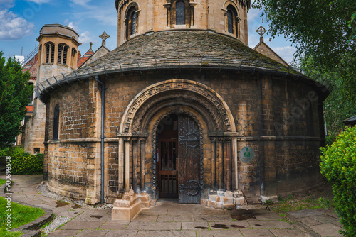 Fotografía The Round Church, or Church of the Holy Sepulchre, in Cambridge, UK, features a rare circular design, conical roof, and carved arched entrance, surrounded by greenery