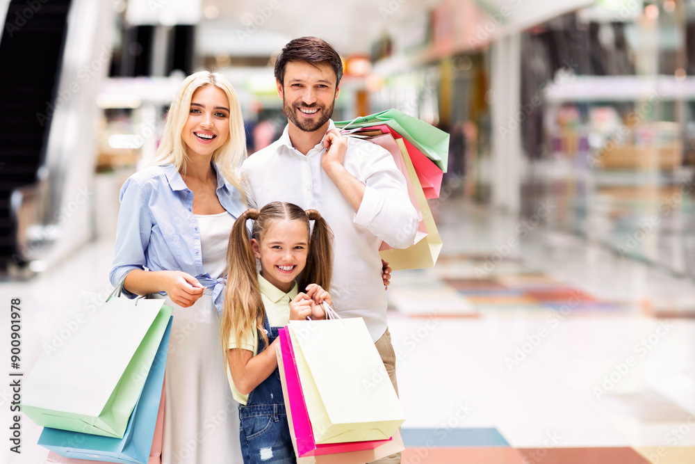 A young family, consisting of a father, mother, and daughter, are standing together in a modern mall, all smiling and holding colorful shopping bags. A young family, consisting of a father, mother, and daughter, are standing together in a modern mall, all smiling and holding colorful shopping bags.