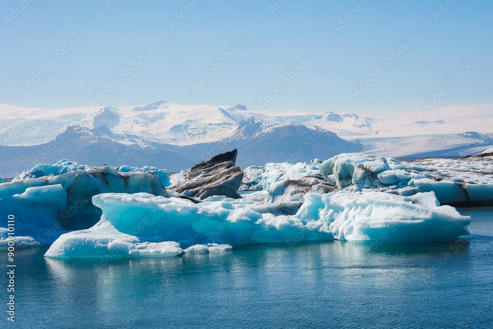 Stunning view of Jokulsarlon Glacier Lagoon in Iceland, featuring blue-tinted icebergs and the majestic Vatnajokull glacier under a bright blue sky.