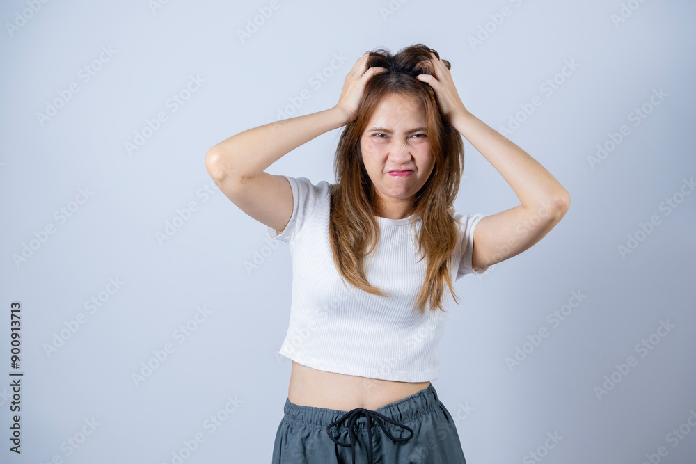 Frustrated woman pulling her hair, expressing stress and anxiety, wearing casual clothes and standing against a white background.