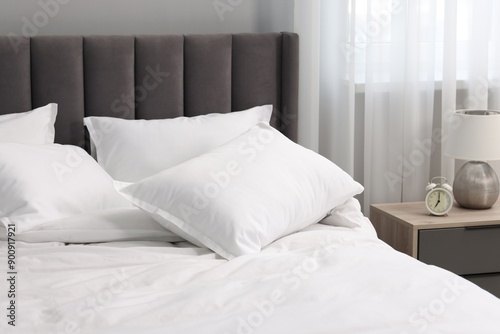 Many soft pillows on bed and bedside table at home