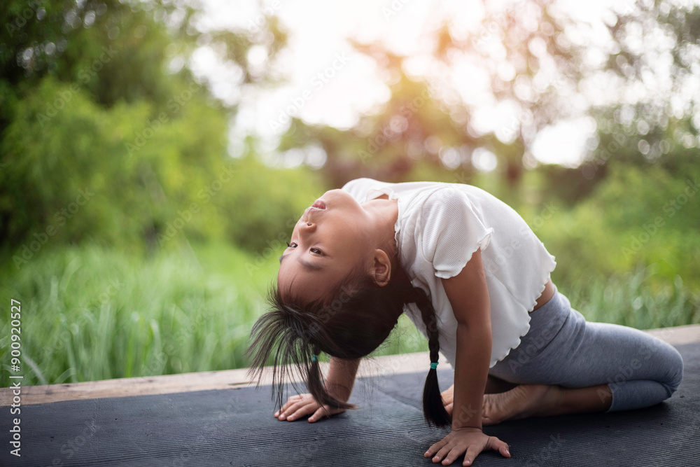 A little girl practices yoga in the backyard, surrounded by the refreshing embrace of nature. A little girl practices yoga in the backyard, surrounded by the refreshing embrace of nature.
