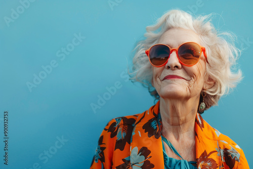 Happy smiling senior woman wearing sunglasses, blue solid colorful background, image with space for text / Femme âgée souriante et heureuse avec lunettes de soleil, fond bleu, espace pour le texte photo