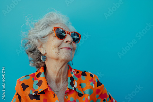 Happy smiling senior woman wearing sunglasses, blue solid colorful background, image with space for text / Femme âgée souriante et heureuse avec lunettes de soleil, fond bleu, espace pour le texte photo