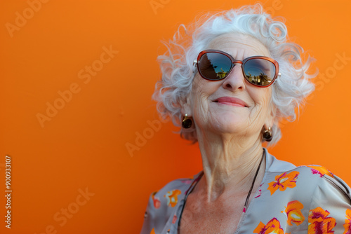Happy smiling senior woman wearing sunglasses, orange solid colorful background, image with space for text / Femme âgée souriante et heureuse avec lunettes de soleil, fond orange, espace pour le texte