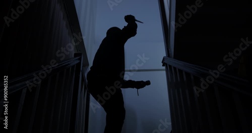 A thief in a black cloak and gloves sneaks into a house at midnight, holding a knife and flashlight, with the intent to harm the occupants.