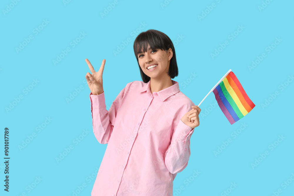 Beautiful young woman with LGBT flag showing victory gesture on blue background Beautiful young woman with LGBT flag showing victory gesture on blue background