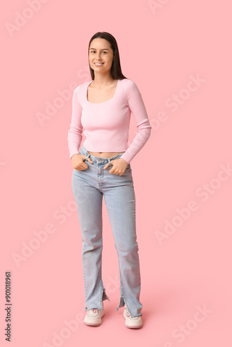 Beautiful young woman in stylish jeans on pink background