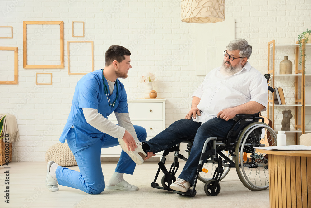 Young caregiver taking care of senior man in wheelchair at home