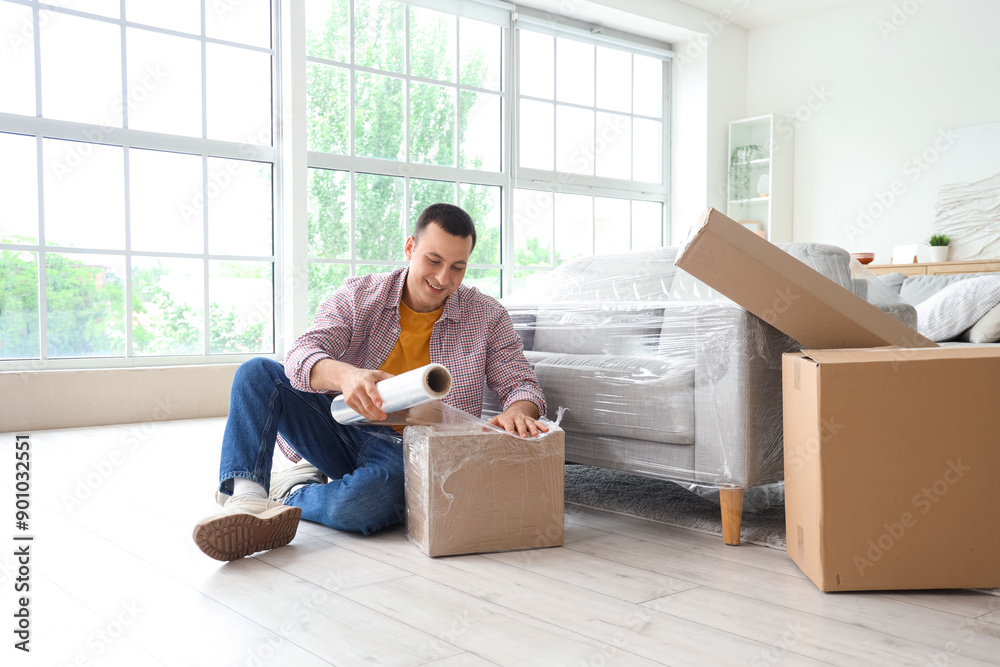 Young man wrapping box with stretch film at home Young man wrapping box with stretch film at home