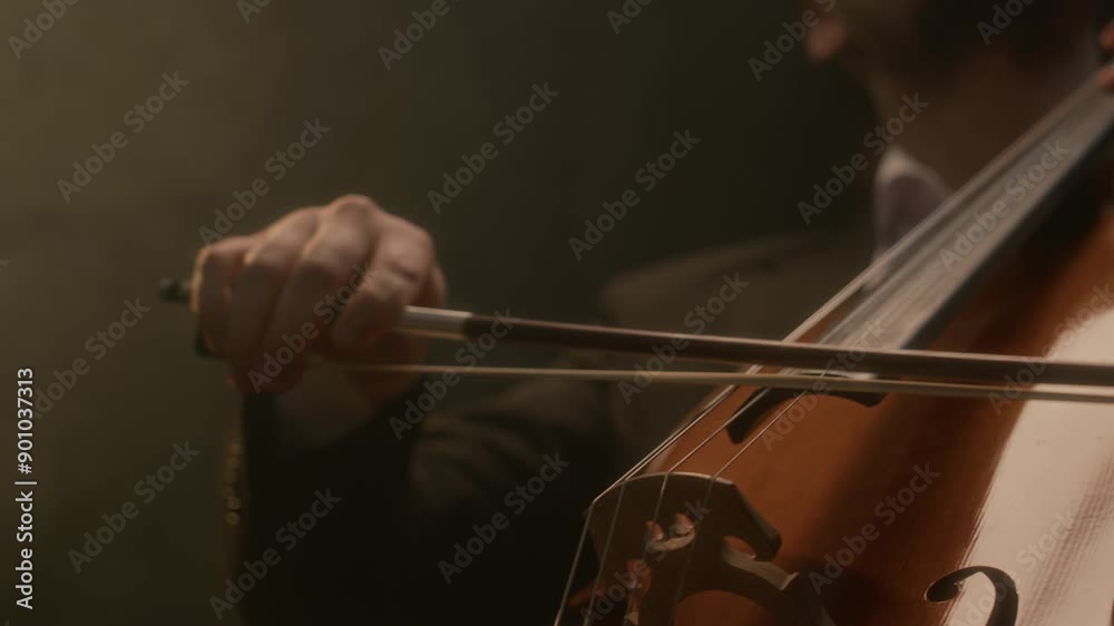 Cropped shot of unrecognizable male musician in suit performing music with cello on black background