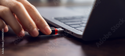 Hand holding usb flash drive with connecting to laptop at wooden table