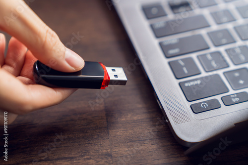 Hand holding usb flash drive with connecting to laptop at wooden table
