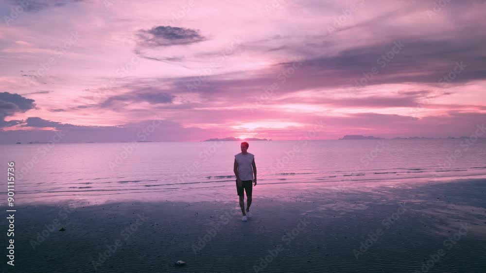 Caucasian male traveler walks along the beach in the evening against the backdrop of a beautiful purple sunset on the sea. Travel concept. Sea holiday, Exotic Beach Destination Caucasian male traveler walks along the beach in the evening against the backdrop of a beautiful purple sunset on the sea. Travel concept. Sea holiday, Exotic Beach Destination